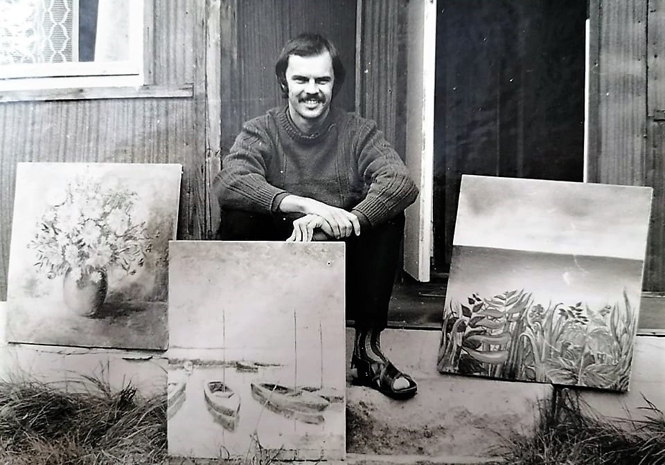 Archiwalne czarno-białe zdjęcie Zygmunta Jasnocha stojącego w progu domu, otoczonego swoimi wczesnymi obrazami sprzed około 30 lat.
